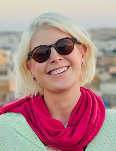 Smiling woman with short blonde hair wearing sunglasses and a red scarf outdoors